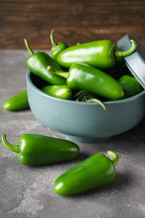 Green jalapeno peppers in a ceramic bowl on a gray background, close-up, vertical.の写真素材