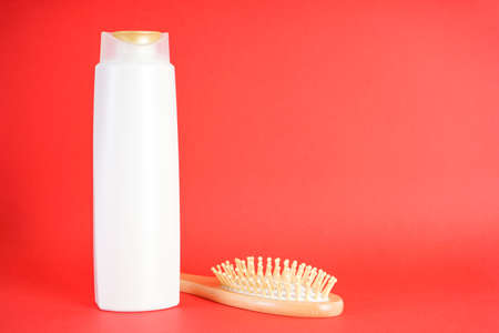 Shampoo bottle and wooden hair brush on red background. Space for text.