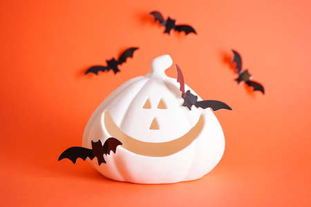 Halloween concept. White halloween pumpkin and bats on an orange background.