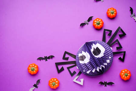 Halloween decorations, paper spider and bats with pumpkins on purple background, space for text, flat lay.の写真素材