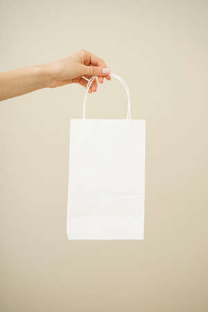 Paper yellow bag, eco packaging in a female hand on a beige background, space for text.