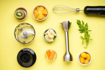 Hand blender and accessories with sliced fruit on a yellow background. Flat lay.の写真素材