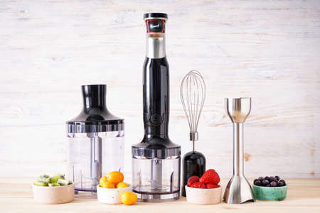 Black plastic electrical hand blender and accessories with fruit on wooden background.の写真素材