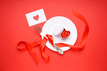 Stylish table setting and gift for Valentine's Day on a red background. top view.の写真素材