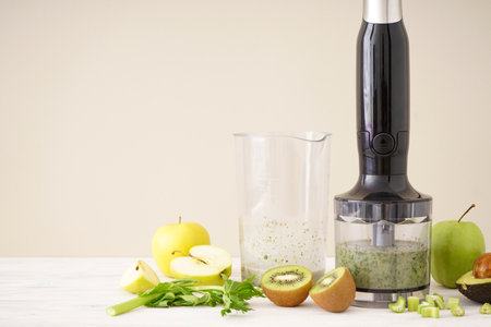 Black plastic electrical hand blender and accessories with sliced fruit on wooden background, place for text.の写真素材