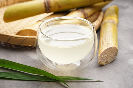 Fresh sugar cane juice in glass on a gray background, closeup.