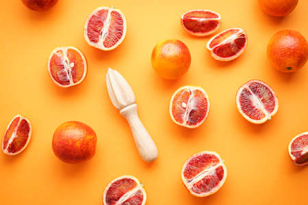 Ripe blood oranges sliced and whole with wooden juicer on a orange background, top view.の写真素材