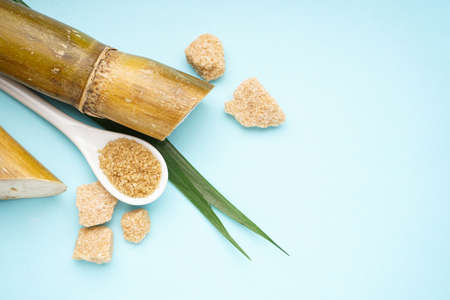 Sugar cane and brown sugar pieces on blue background with space for text. top view.