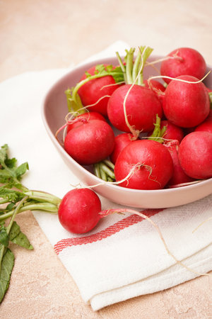 Fresh red radishes in a ceramic bowl over beige surface. close-up. vertically.の写真素材