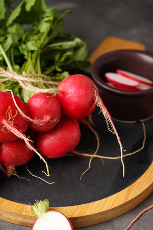 Fresh red radish with leaves on cutting board on gray background, vertically. close-up.の写真素材