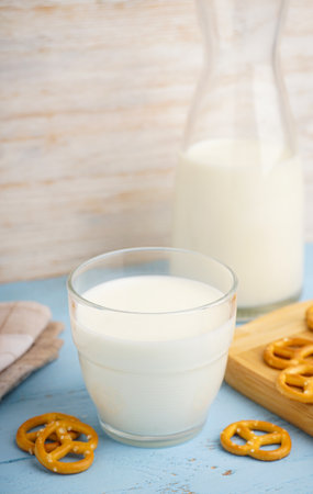 Glass and jug of fresh milk on wooden table against color background, with cookies.の写真素材