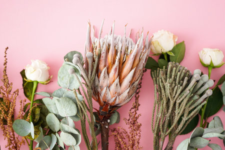 Bouquet with white roses, protea, brunia and eucalyptus branches on a pink background, top view.