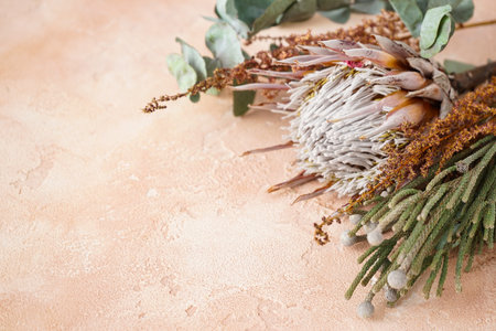Beautiful bouquet with protea, brunia and eucalyptus branches on a beige background with space for text, top view.の写真素材