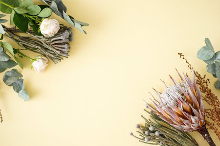 Beautiful bouquet with white roses, protea, green brunia and eucalyptus branches on a yellow background, space for text. Flat lay.の写真素材