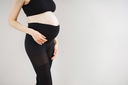 Young pregnant woman in black tights on gray background. Space for text. Expectation time.