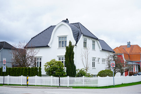 Traditional white wooden Scandinavian house with a distinctive curved roof and black roof tiles. Captured on a cloudy spring day in a quiet residential area in Norway.の写真素材