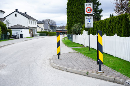 Traffic signs showing a 30 km/h speed limit and parking zone on a quiet Norwegian residential street. Surrounded by white fences, trees, and houses, the image captures the organized and peaceful Scandinavian infrastructure.の写真素材
