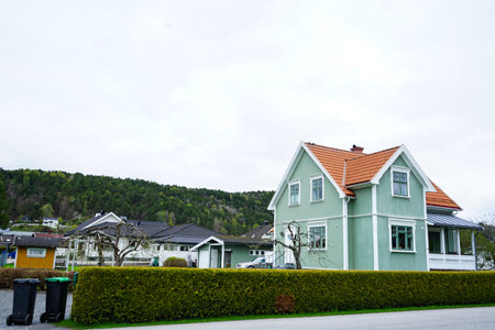 Classic Scandinavian two-story wooden house painted in sage green with a red tiled roof and white...