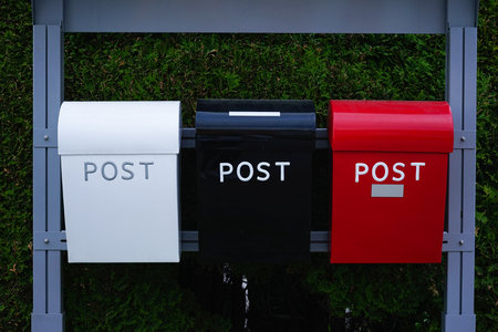 White, black, and red metal mailboxes with the word POST mounted on a metal frame in front of a...