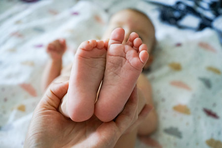 Close-up view of a parent's hand gently holding the soles of a baby's tiny feet, showing delicate...
