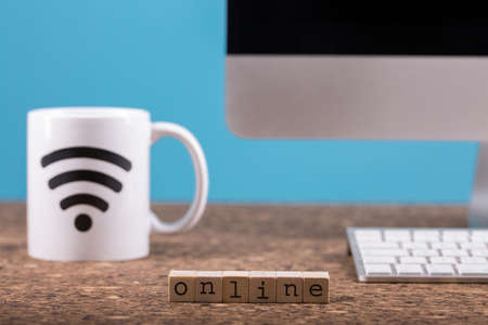 Close up view of a cork work desk interior with a computer, a mug of coffee with the sign connected,...