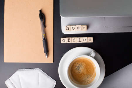 Close up view of a black work desk interior with a laptop computer, a cup of coffee, paper, pen, plant, face mask for coronavirus black backgroundの写真素材