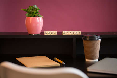 Close up view of a black work desk interior with a laptop computer, a cup of coffee, paper, pen, plant and pink background.の写真素材
