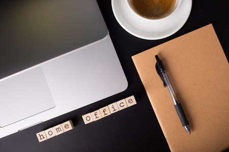 Close up view of a black work desk interior with a laptop computer, a cup of coffee, paper, penの写真素材