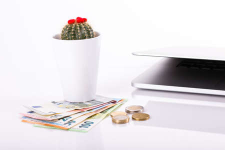 pile of paper and metal euro banknotes and coins on a white background on a desktop with computer and coffee mug. Â© Michele Agostinis / Visualbrand Photographyの写真素材
