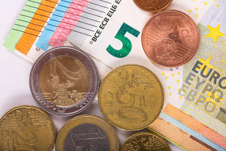 pile of paper and metal euro banknotes and coins on a white background as part of the united...