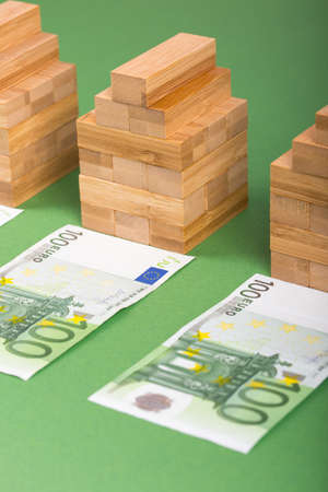 Three houses, three 100 euros banknotes and green background. Concept for real estate marketの写真素材