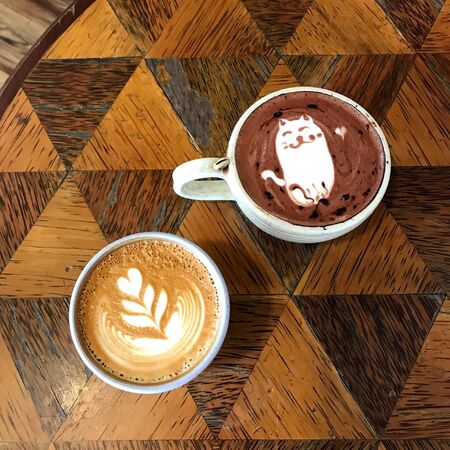 two coffee milk and chocolate in a white cup on a wooden tableの写真素材
