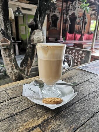 coffee milk in a long glass with one biscuit on a wooden tableの写真素材