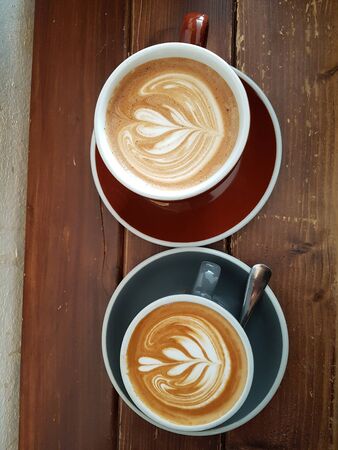 two milk coffees in the shape of a tree in a cup on a wooden tableの写真素材