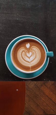 coffee milk with a heart shape in a blue cup on a wooden tableの写真素材