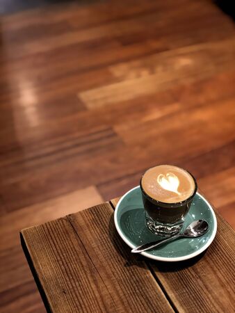 cappuccino coffee with heart shape in a blue glass on the tableの写真素材
