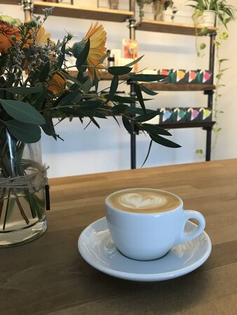 Coffee milk with a heart shape in a cup with a cafe and plant backgroundの写真素材