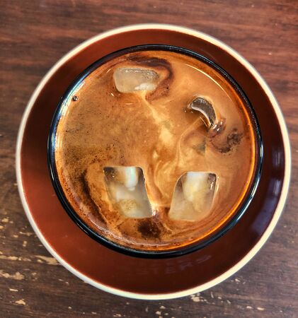 milk coffee with ice cubes in a glass on the tableの写真素材