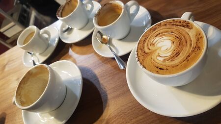 one cappuccino with cocoa powder and four cups with finished cappuccinoの写真素材
