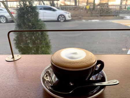 milk coffee with cream in the middle in a white cup with a street backgroundの写真素材