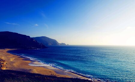 green and sea blue and sky blue beautiful sea and sunset with large yellow sun under the sea surface hills in the background.の写真素材