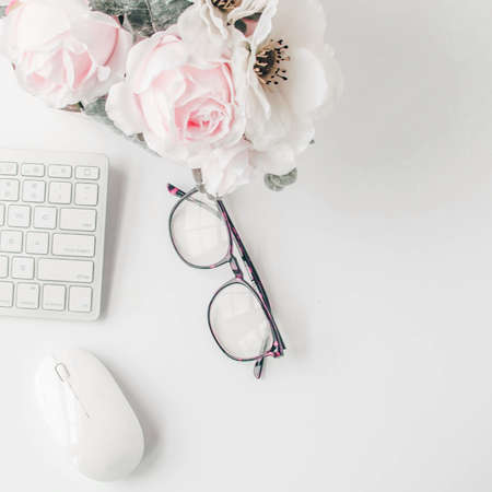 white workspace with light pink note book and white flower with coffee on white table background.