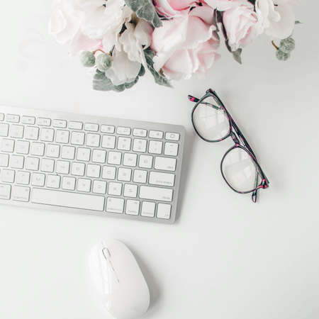 white workspace with light pink note book and white flower with coffee on white table background.