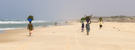 Woman walking while carrying baskets on the head on a Senegalese beach