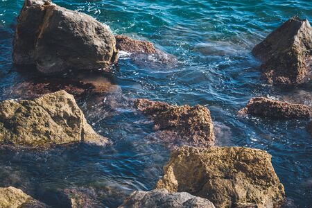 Rough rocks sticking out of transparent rippling water of blue sea on a sunny dayの写真素材