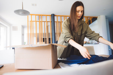 Caucasian woman taking the clothes from her online order out of the box, looking if she wants to...
