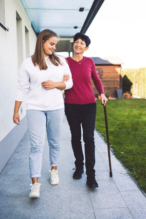 Senior woman walking with a cane in one arm and holding for nurses hand on the otherの写真素材