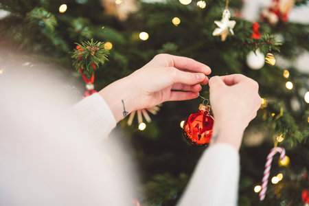 Unrecognizable woman hands decorating the Christmas tree with red ornamentsの写真素材