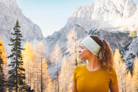Waist up caucasian woman hiker looking at the side, with mountains and forest in the backgroundの写真素材