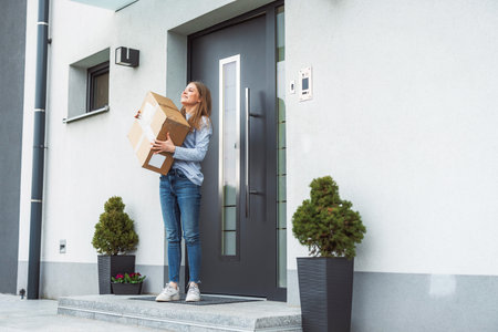 Smiling young woman receiving an early Christmas present, hugging the box, standing at the front doorの写真素材